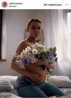 a woman sitting on top of a bed holding flowers