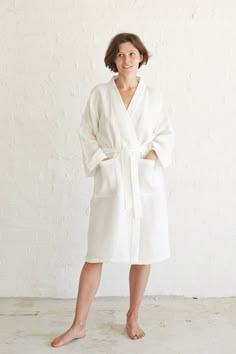 a woman standing in front of a white wall wearing a robe and pink slippers