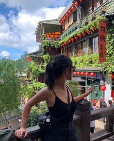 a woman is standing on a balcony looking at the buildings with red lanterns hanging from them