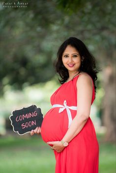 a pregnant woman in a red dress holding a chalkboard with the words coming soon written on it