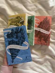 three harry potter books on a bed with white sheets in the foreground, and a person's hand holding one