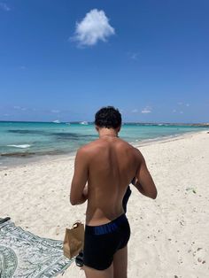 a man standing on top of a sandy beach next to the ocean in swim trunks