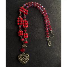 a red beaded necklace with a heart and tree charm hanging from it's side