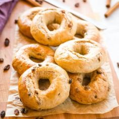 several bagels sitting on top of a wooden cutting board next to a knife and some raisins