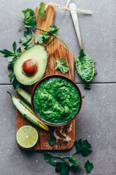 an avocado dip in a bowl surrounded by sliced cucumbers and cilantro