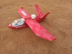 a small red airplane laying on top of a dirt field