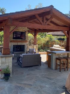 an outdoor kitchen and living area with stone flooring, wood pergolated roof and fireplace