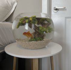 a fish bowl sitting on top of a white table next to a bed with pillows