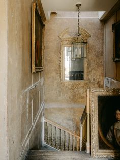 a staircase with paintings on the wall and a mirror hanging from the ceiling above it