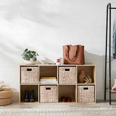 a shelf with baskets and shoes on it in front of a white wall, next to a coat rack