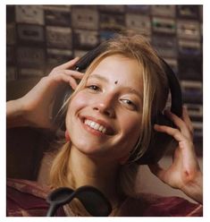 a woman smiling and listening to headphones in front of a wall of sound equipment