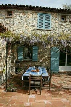 an outdoor table and chairs in front of a stone building with blue shutters on the windows