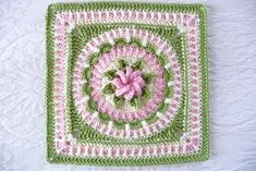 a crocheted square with a pink flower in the center on a white surface