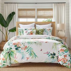 a tropical themed bed with white sheets and green leaves on it, in front of a window