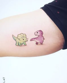 a woman's arm with two cartoon dinosaurs on it, one is pink and the other is green