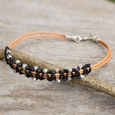 a leather bracelet with silver beads on top of a piece of driftwood next to a wooden stick