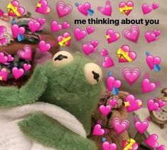 a green stuffed animal sitting on top of a bed with hearts flying out of it