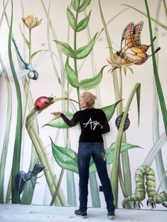 a woman standing in front of a mural with bugs and butterflies painted on the wall