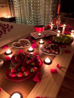 a wooden table topped with lots of plates and bowls filled with fruit next to candles