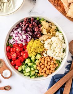 a large bowl filled with different types of vegetables and chickpeas next to wooden spoons