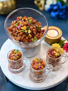 three cups filled with food sitting on top of a white plate next to a candle