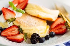 a plate topped with pancakes covered in powdered sugar and berries next to strawberries