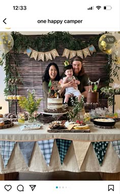 two people and a baby sitting at a table in front of a banner with the words happy camper on it