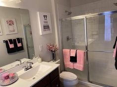 a bathroom with a sink, toilet and shower in it's center area that has pink towels hanging on the wall