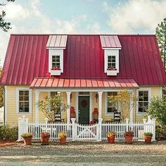 a small yellow house with a red roof and white picket fence around the front porch