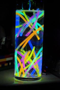 a glass filled with neon colored sticks on top of a table