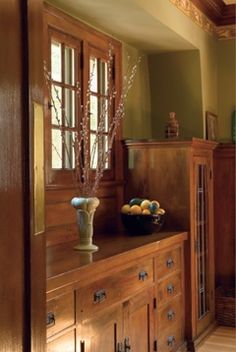 a bowl of fruit sitting on top of a wooden cabinet next to a vase filled with flowers