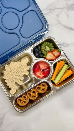 a bento box filled with fruit, pretzels and crackers on a marble countertop