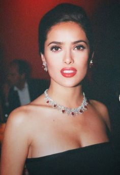 a woman in a strapless dress wearing a necklace and earrings with red lipstick on her lips