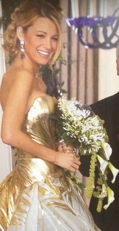 a woman in a gold and white dress holding a bouquet with an older man standing next to her