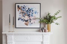 a white fireplace mantel topped with a painting and two vases