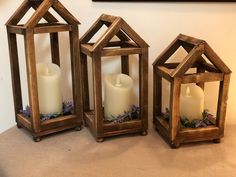 three wooden lanterns with white candles in them sitting on a table next to a wall