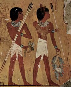 two ancient egyptian men holding spears and wearing headdress, painted on the side of a wall