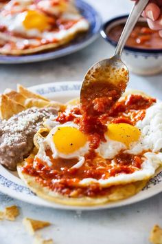 a person is spooning eggs over some food on a plate with tortilla chips