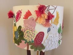 a lampshade decorated with colorful birds and flowers on a wooden stand next to a white wall