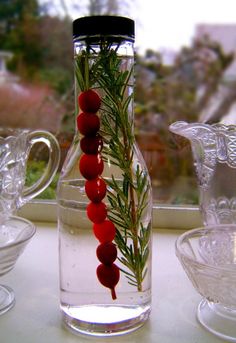 a glass bottle filled with water and red beads next to other glass bowls on a window sill