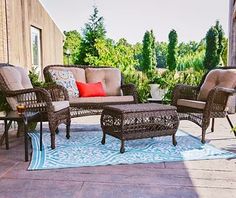 an outdoor patio with wicker furniture and colorful pillows on the rug, in front of a house