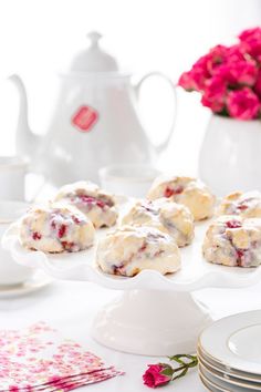 a table topped with plates and cups filled with pastries on top of a white cake stand