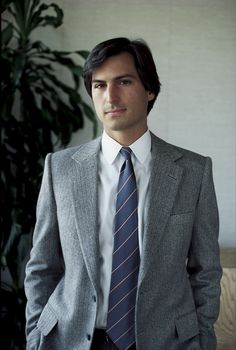 a man wearing a suit and tie standing in front of a plant