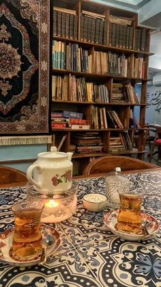 two tea cups on a table in front of a bookshelf filled with books