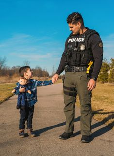 a police officer is holding the hand of a little boy who is standing on a road