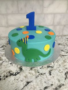 a birthday cake with the number one on it and a green dinosaur holding a party hat