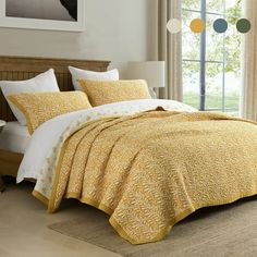 a bed with yellow comforter and pillows in a room next to a window,