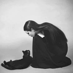 a woman is sitting on the floor with her black cat and looks at it's tail