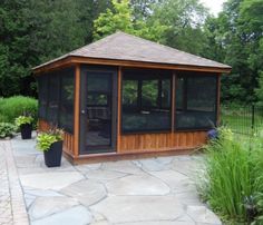 a wooden gazebo sitting on top of a stone patio next to plants and trees