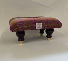 the foot stool is made out of wood and has a colorful plaid pattern on it